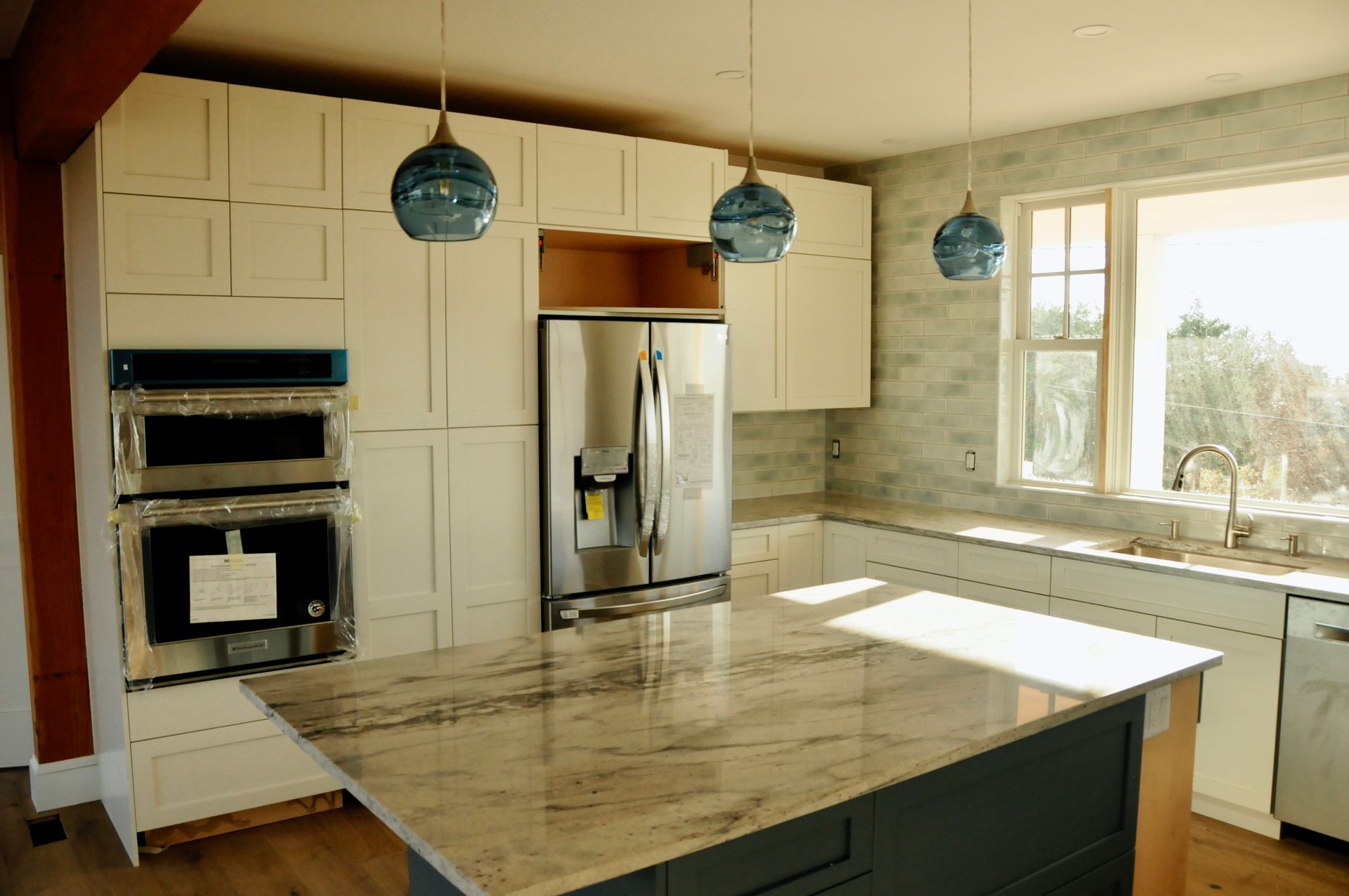 Remodeled kitchen with a marble-top island, blue glass pendant lights, and stainless appliances